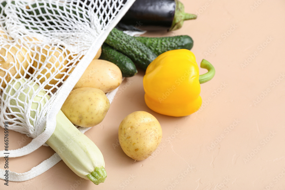 Mesh bag with different fresh vegetables on beige background, closeup