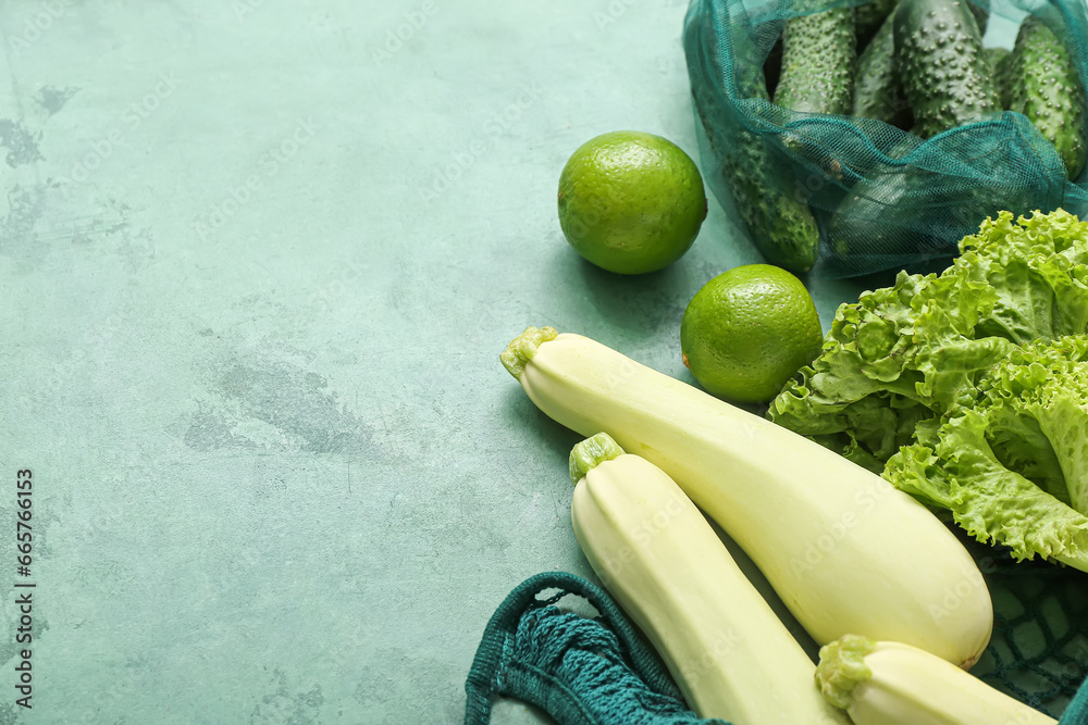 Mesh bags with different fresh vegetables on green background