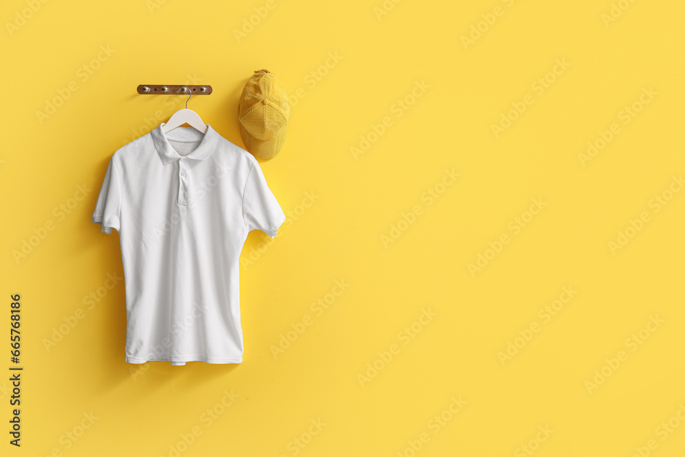 Stylish white t-shirt and cap hanging on yellow background