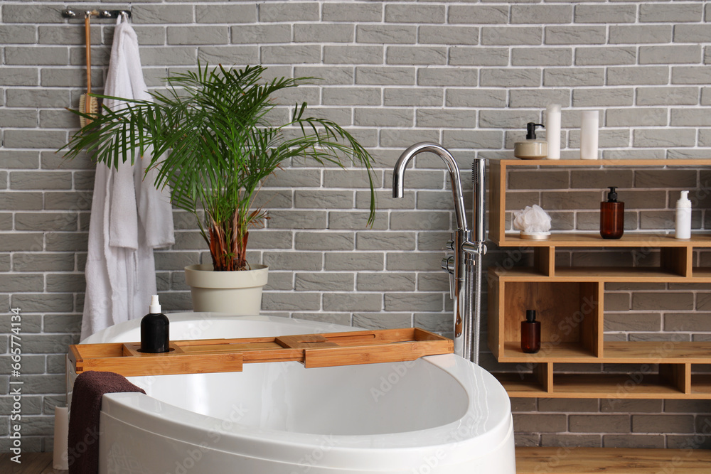 Interior of modern bathroom with bathtub, board and wooden shelving unit