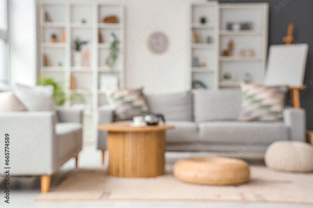 Blurred view of living room with sofas, table and poufs