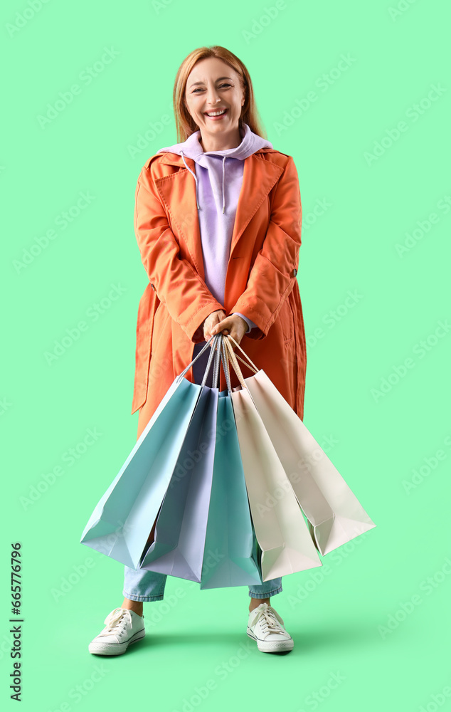 Mature woman in coat with shopping bags on green background