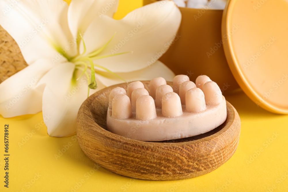 Wooden bowl with massage soap and beautiful lily flower on yellow background, closeup