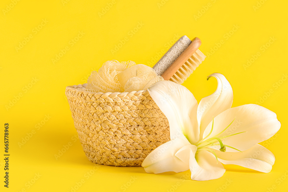 Basket with bath sponge, massage brush and lily flower on yellow background