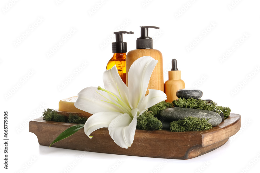 Wooden board with cosmetic products, spa stones and lily flower on white background