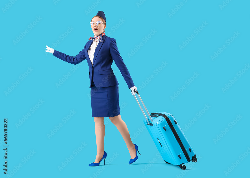 Young stewardess with suitcase on blue background