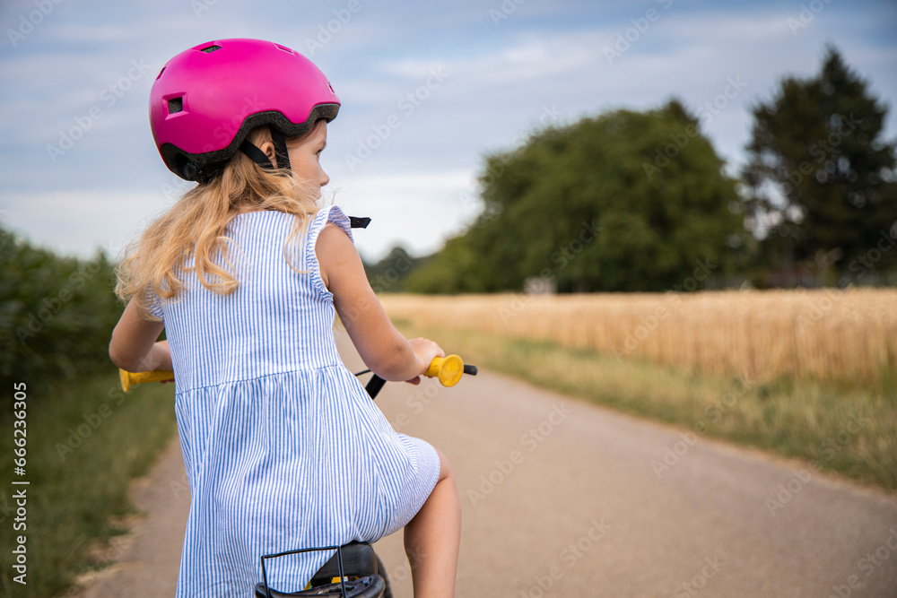 Little child girl in a helmet rides a bike in the field