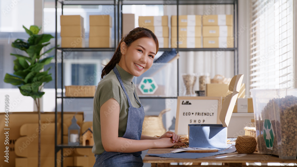 Eco friendly packaging in net zero waste store asian seller retail home office shop. ESG startup Small SME owner young adult woman asia people happy vendor smile carry parcel postal looking at camera.