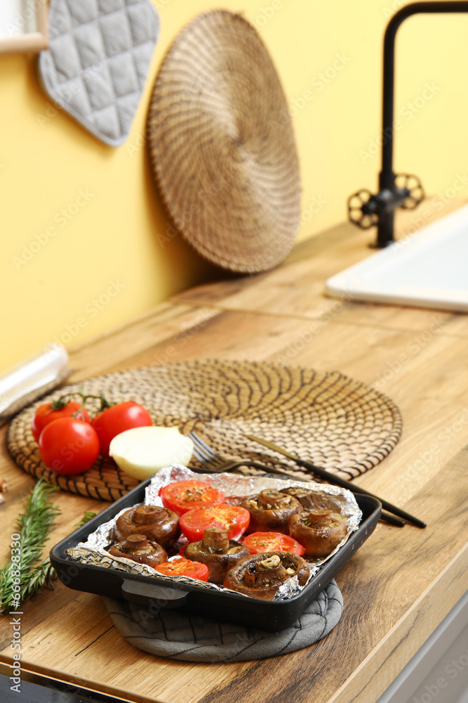 Baking dish with tasty baked mushrooms and tomatoes on wooden table in kitchen