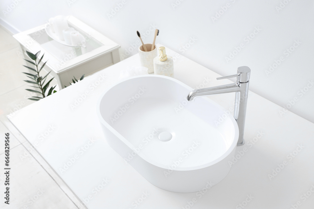 White sink and bath accessories on table in light bathroom, closeup