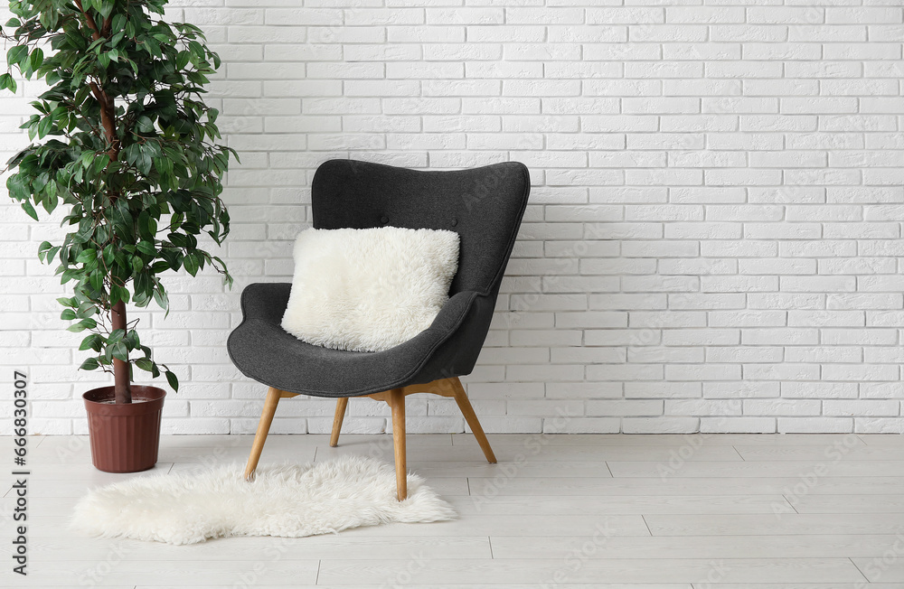 Dark grey armchair with pillow, fluffy rug and houseplant near white brick wall