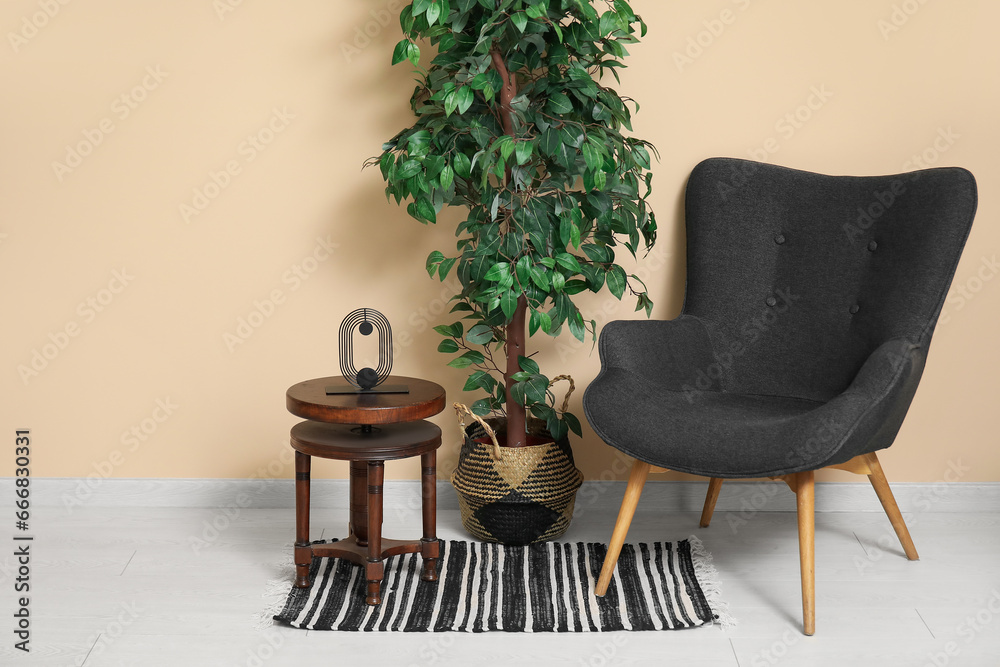 Dark grey armchair with small coffee table, houseplant and rug near beige wall