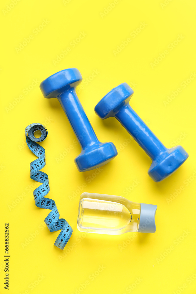 Dumbbells, measuring tape and bottle of water on color background