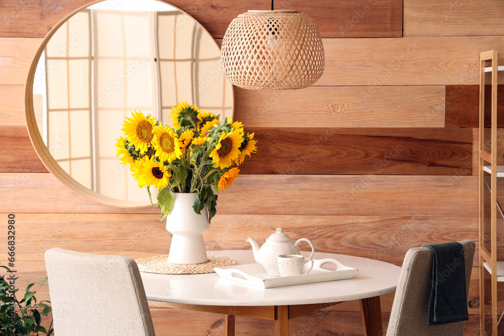 Vase with beautiful sunflowers on dining table with teapot