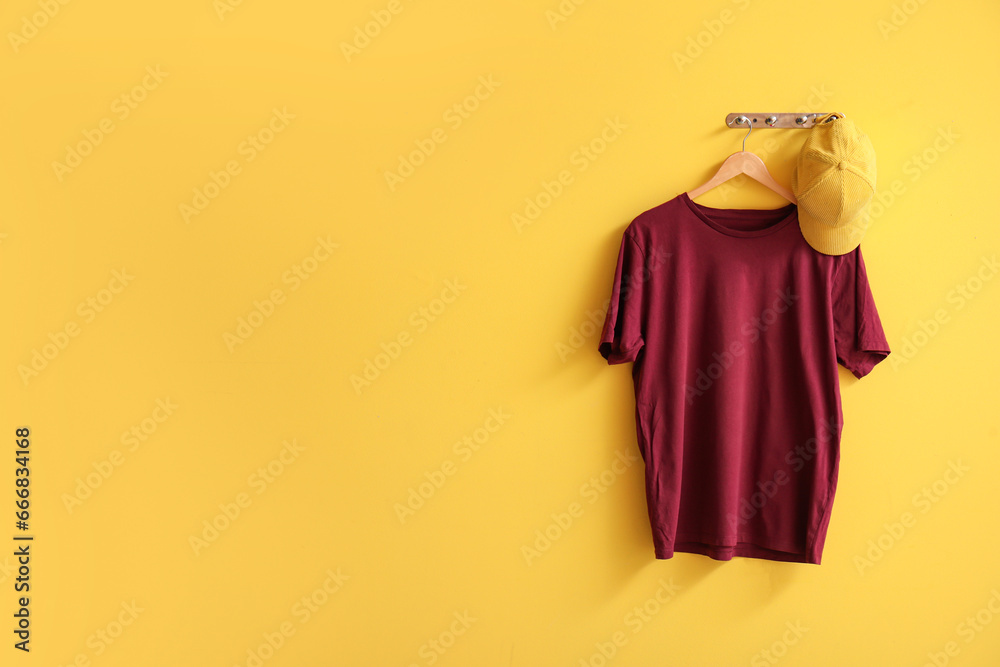 Stylish red t-shirt and cap hanging on yellow background