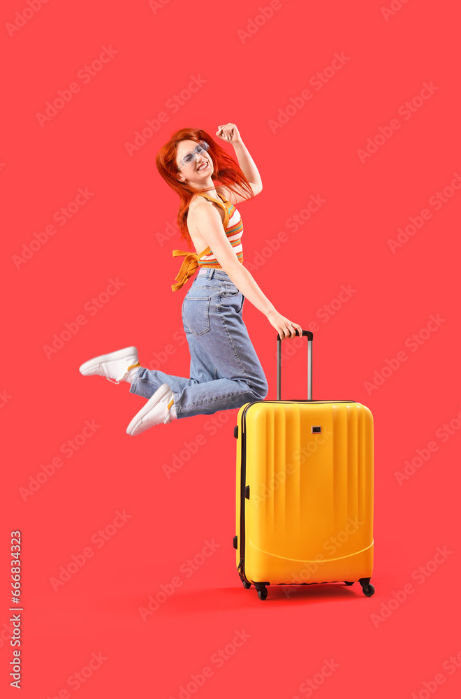 Happy jumping female tourist with suitcase on red background