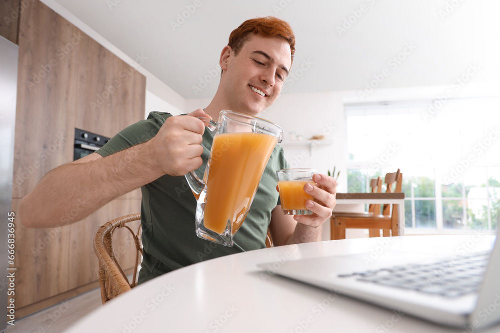 Young man with jug and glass of juice in kitchen