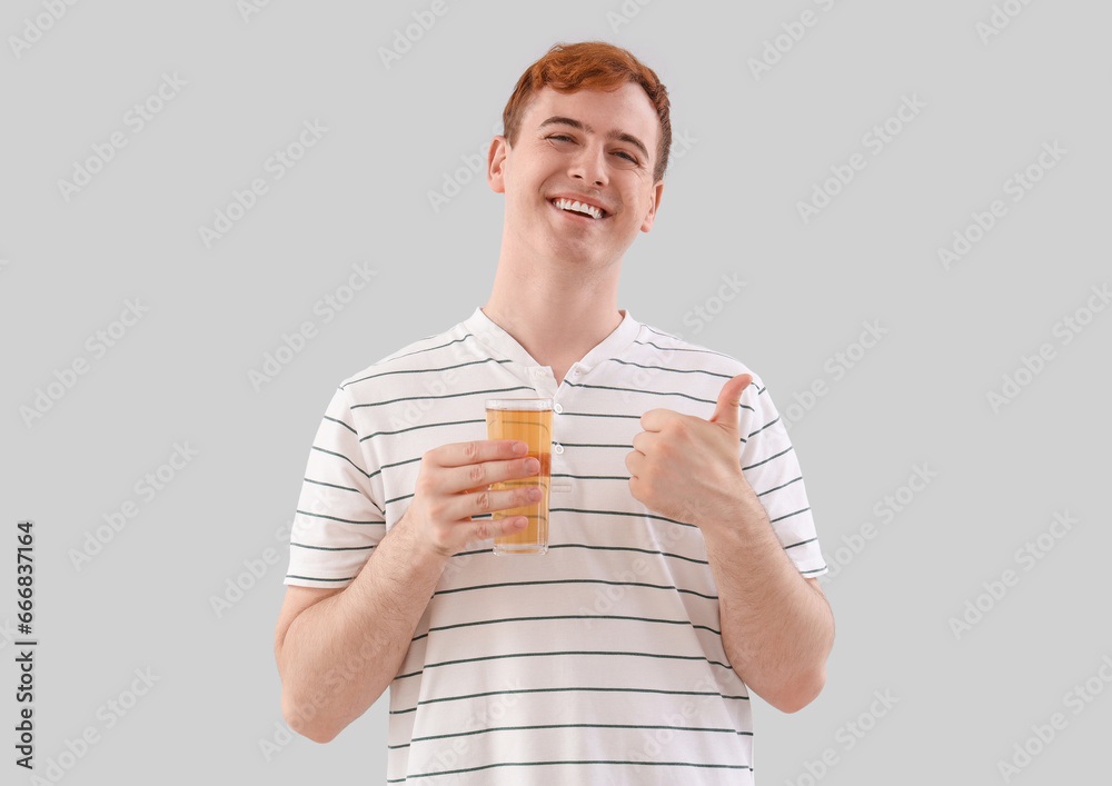 Young man with glass of juice showing thumb-up on light background