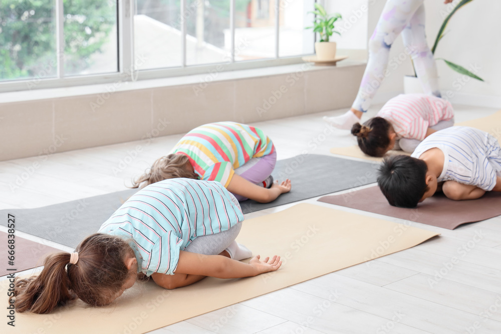 Group of little children practicing yoga with instructor in gym