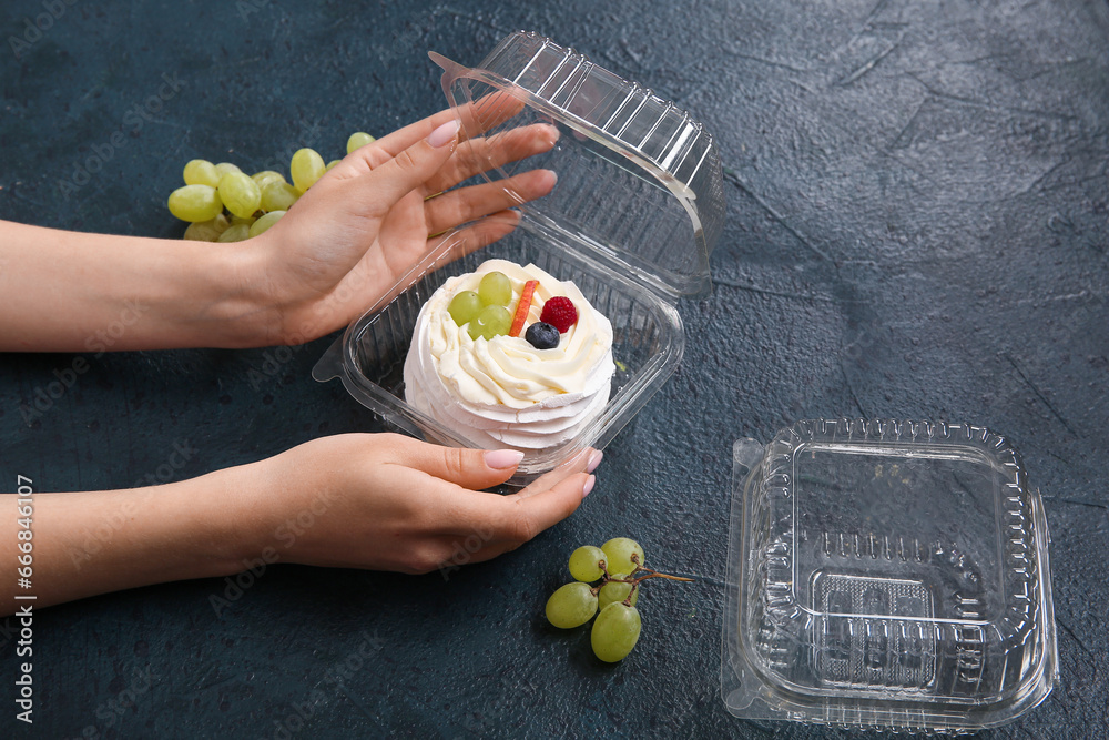 Female confectioner packing tasty cake into plastic container on black background