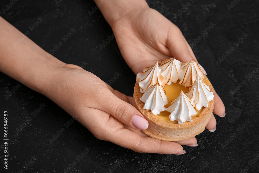 Female confectioner with tasty cake on black background