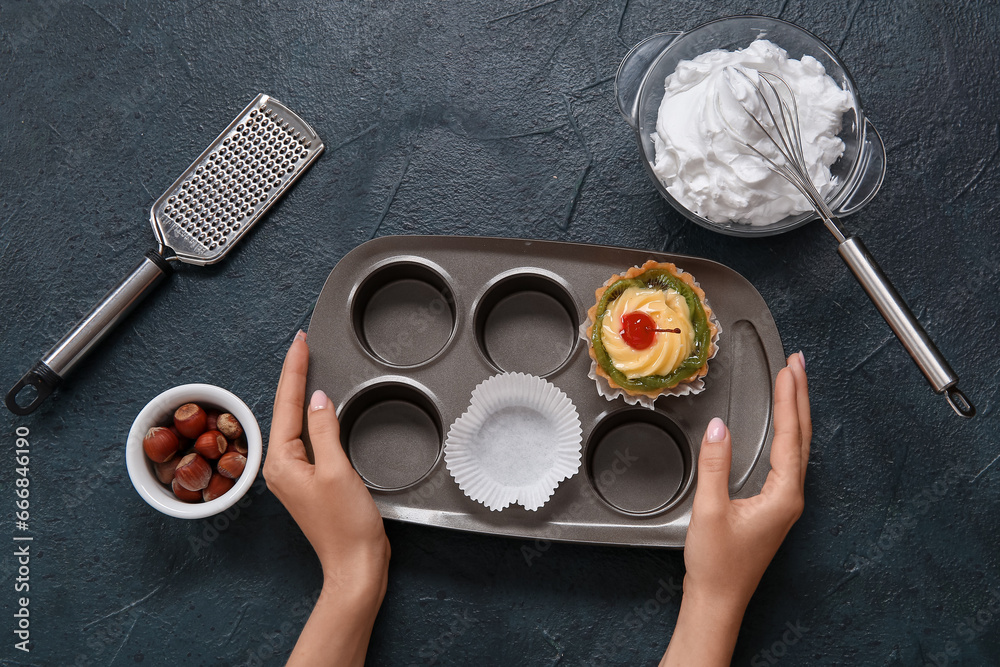 Female confectioner cooking tasty cakes on black background