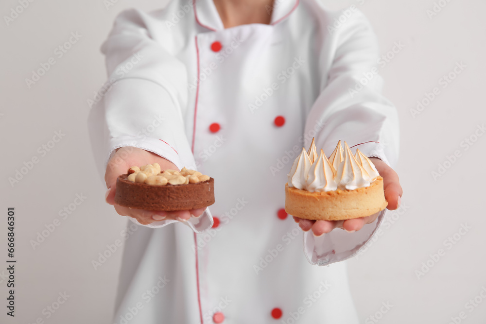 Female confectioner with tasty cakes on white background