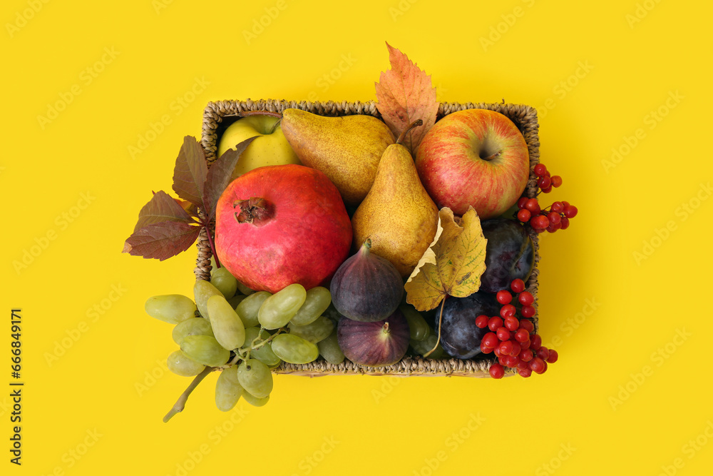 Wicker basket with different fresh fruits on yellow background