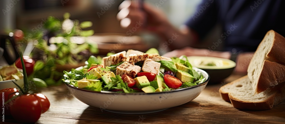 Man eating a healthy salad with chicken avocado sundried tomatoes and baguette during lunch break at a wooden table