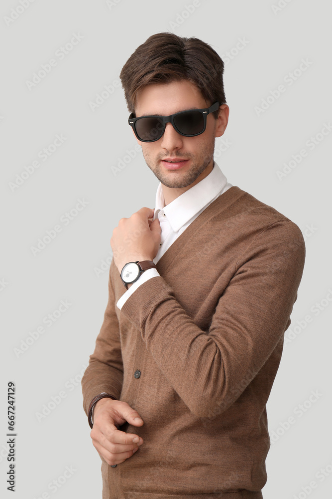 Handsome stylish young man in sunglasses with wristwatch on grey background