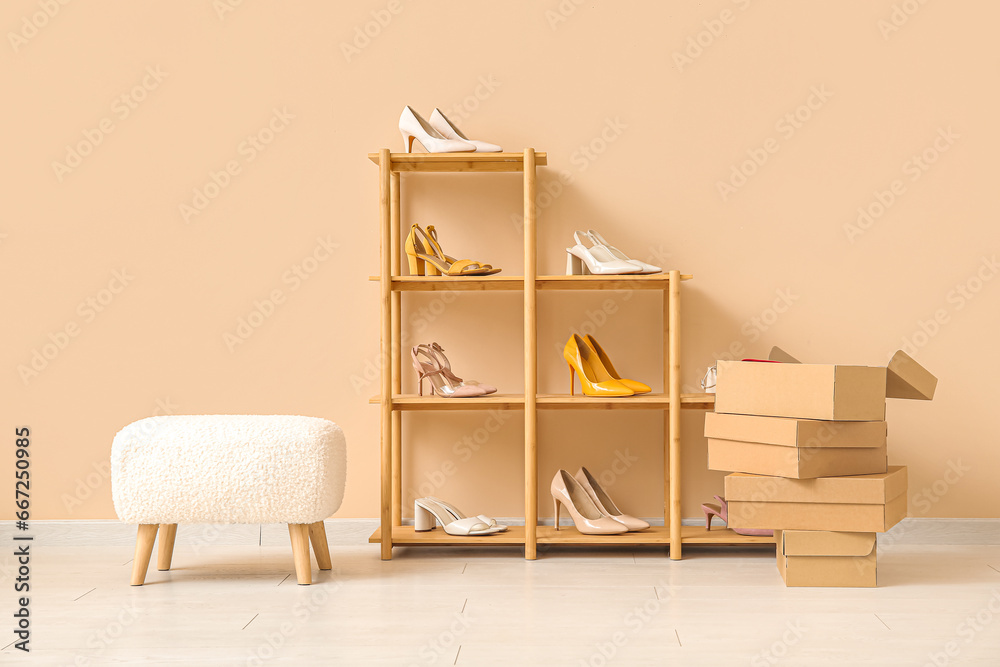 Shelving unit with stylish female shoes, boxes and stool near color wall