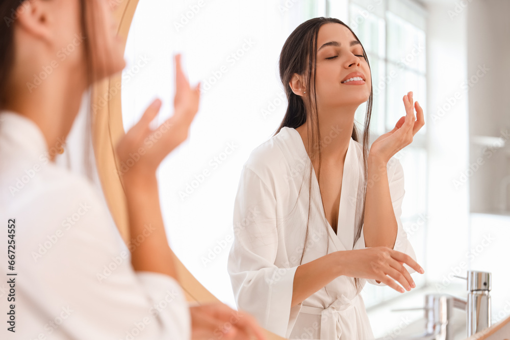 Young woman applying cream near mirror in bathroom