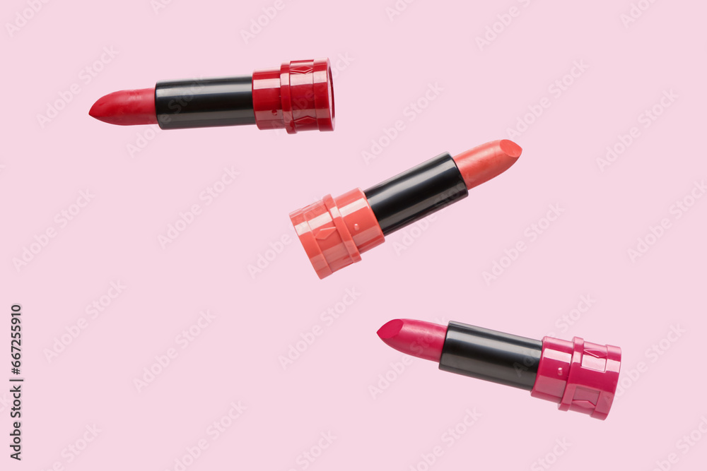 Different lipsticks flying on pink background