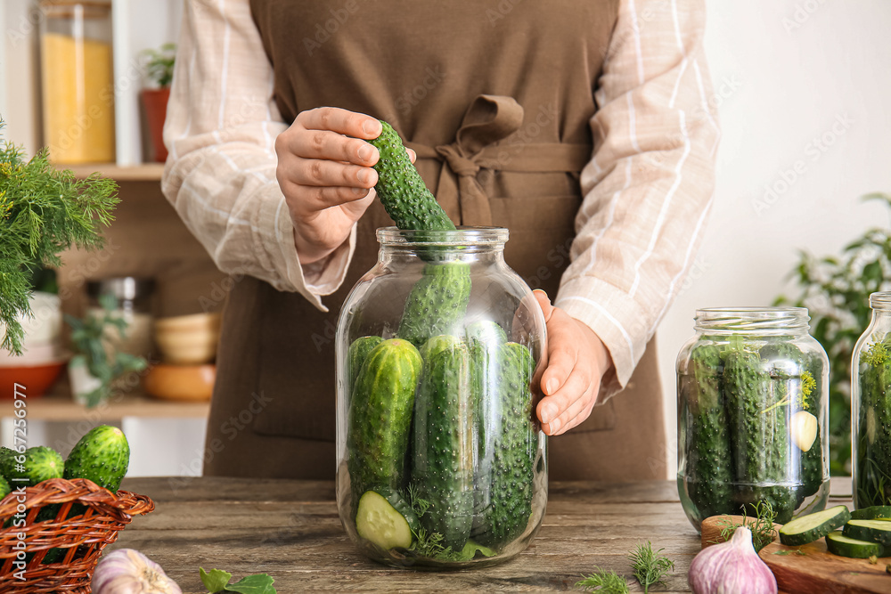 Woman preparing fresh cucumbers for canning at table in kitchen