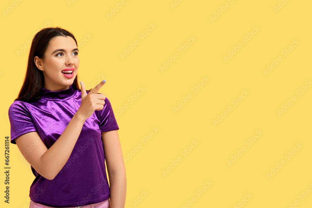 Beautiful young happy woman pointing at something on yellow background