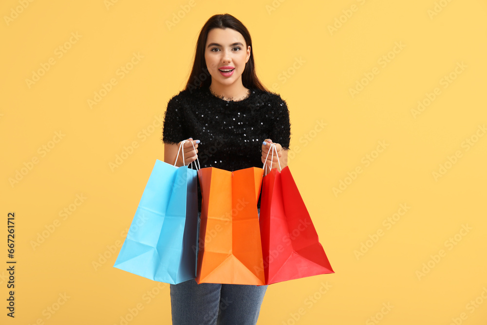 Beautiful young happy woman with shopping bags on yellow background