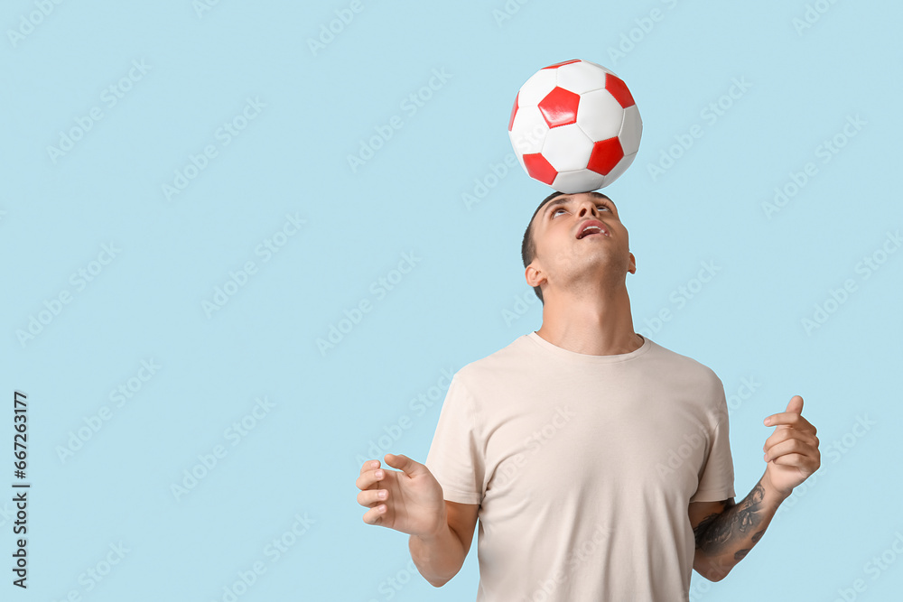 Handsome young man playing with soccer ball on blue background