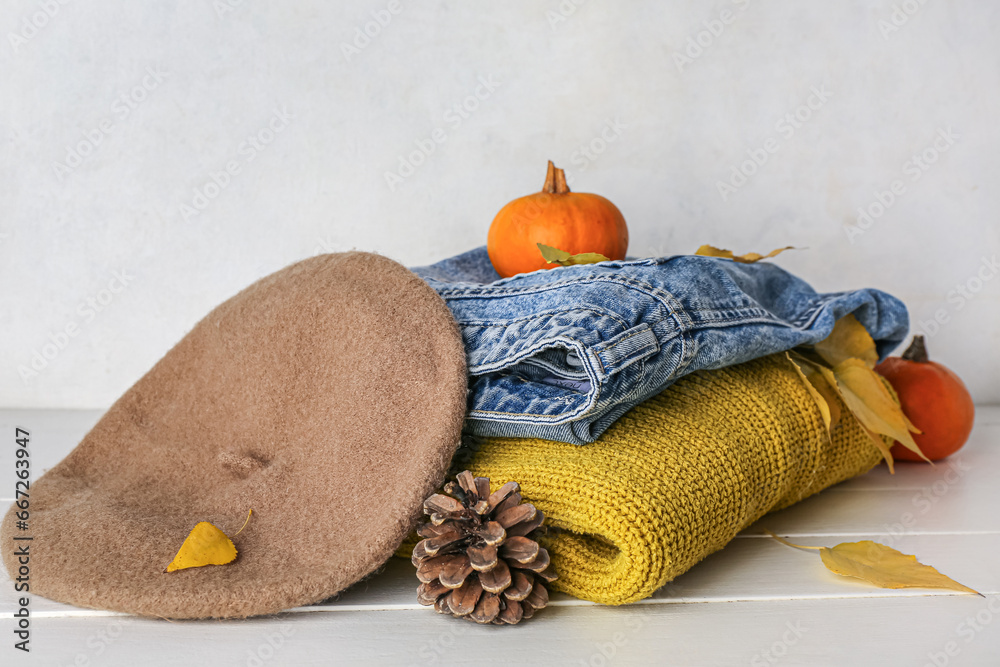 Stylish female clothes, autumn leaves and pumpkins on light wooden table