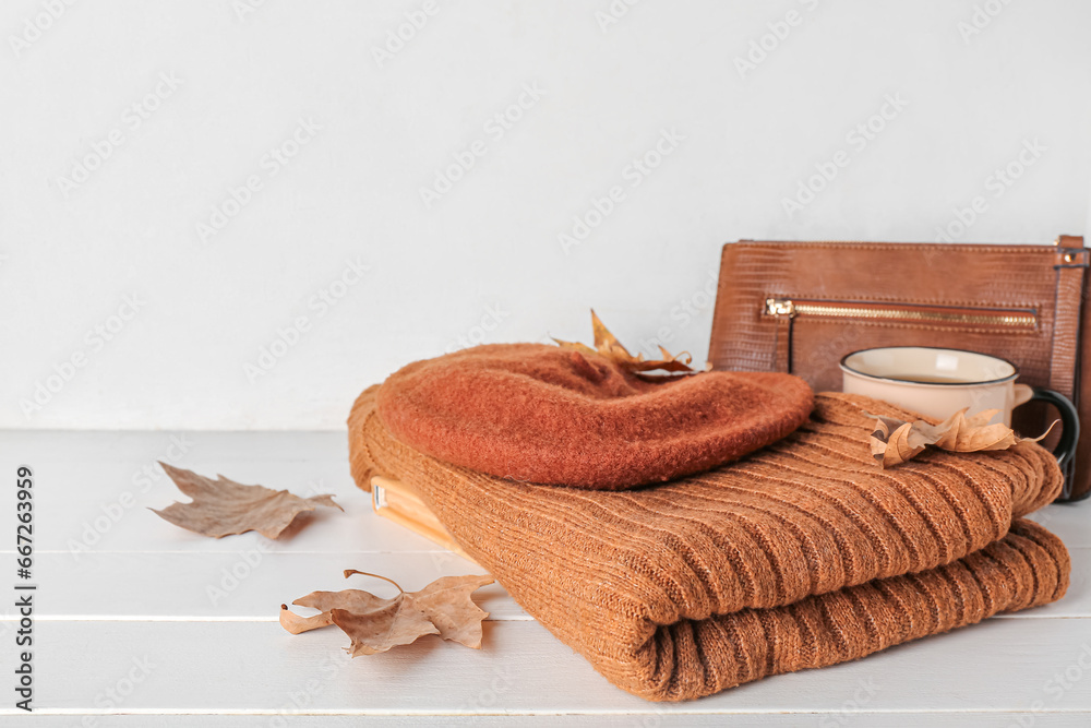 Female clothes, bag, cup of tea and fallen leaves on light wooden table