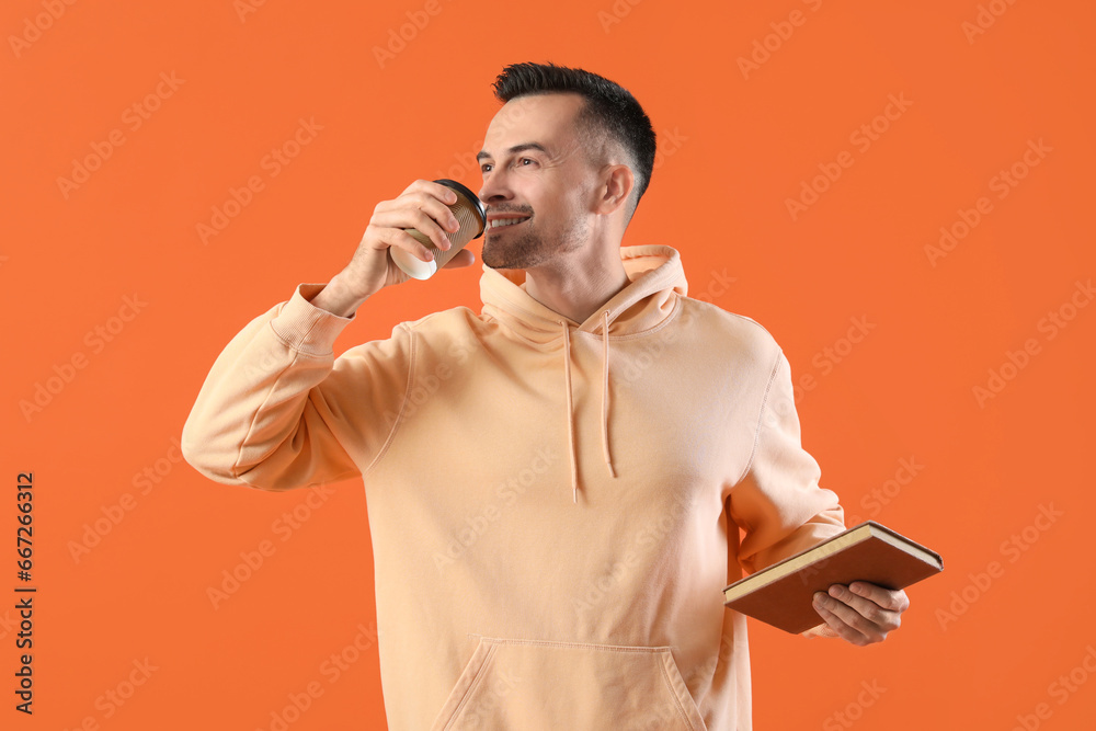 Happy young man with notebook drinking coffee on orange background