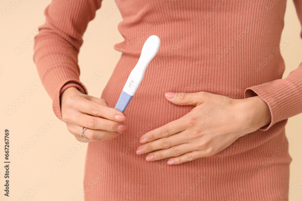 Young woman with pregnancy test on beige background, closeup