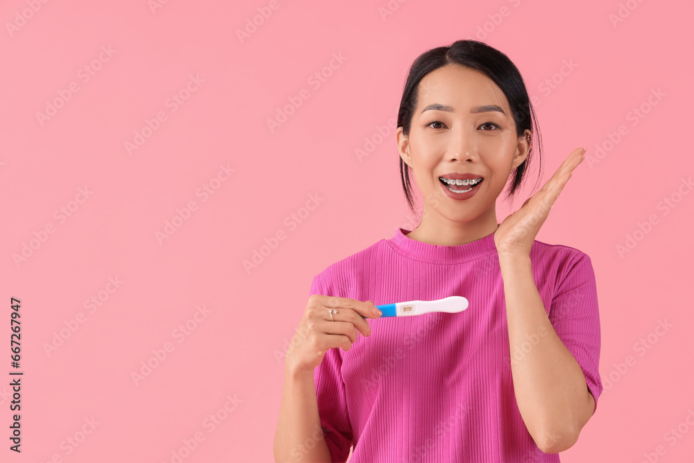 Young Asian woman with pregnancy test on pink background