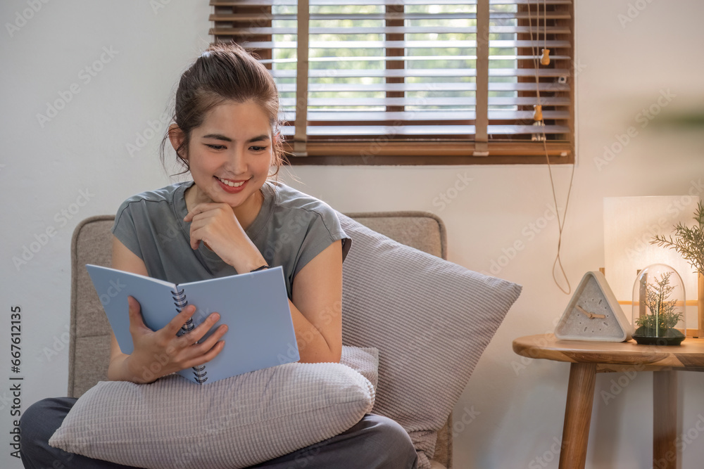 Happy young woman reading book on sofa at home. Lifestyle freelance relax in living room. Lifestyle Concept