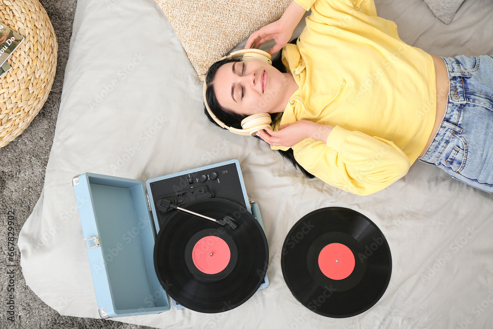 Young woman with headphones and record player in bedroom