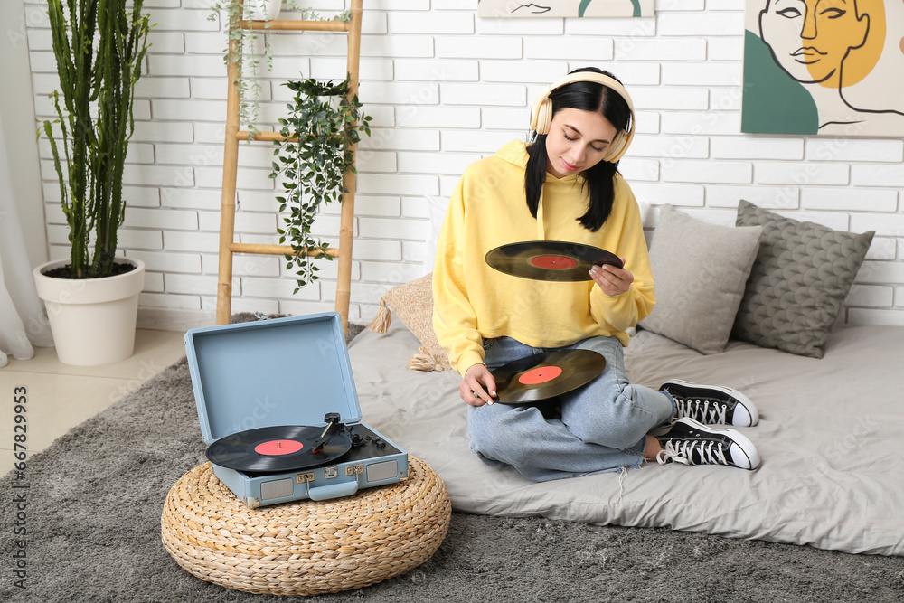 Young woman with headphones and vinyl disks for record player in bedroom