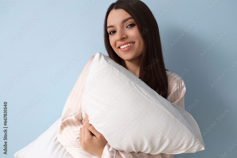 Young woman in pajamas with soft pillow on blue background