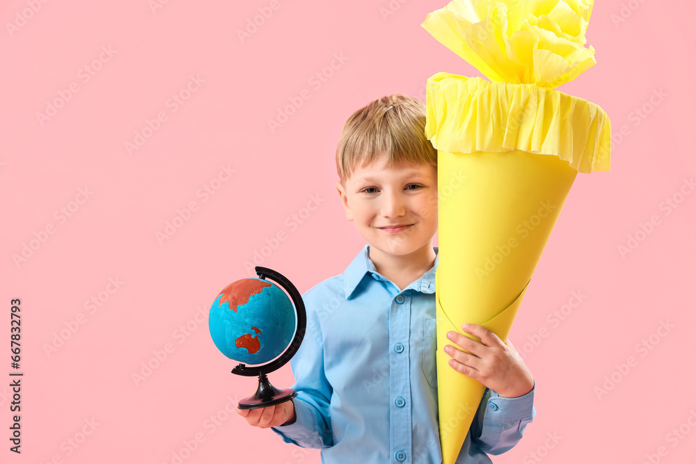 Happy little boy with yellow school cone and globe on pink background