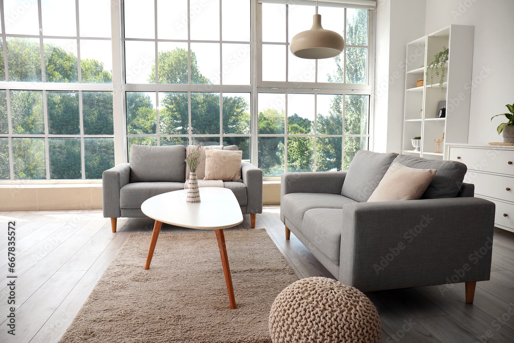 Interior of light living room with cozy grey sofas, coffee table and big window