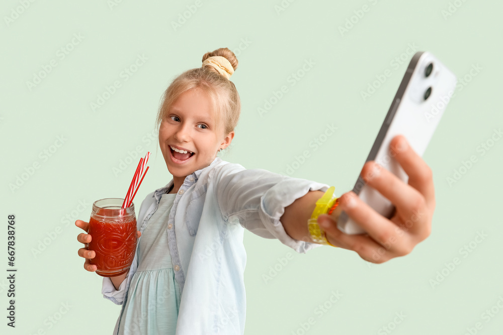 Little girl with glass of juice taking selfie on green background