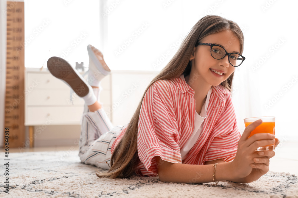 Little girl with glass of juice lying on floor at home